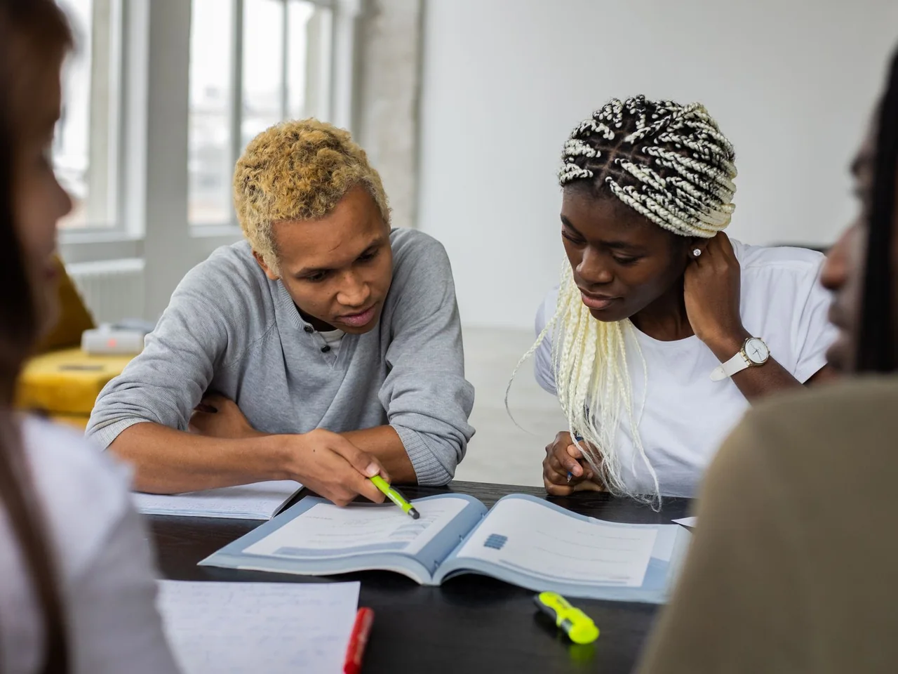 Four young adults studying together around an open textbook; licensed stock photograph, not foundation participants